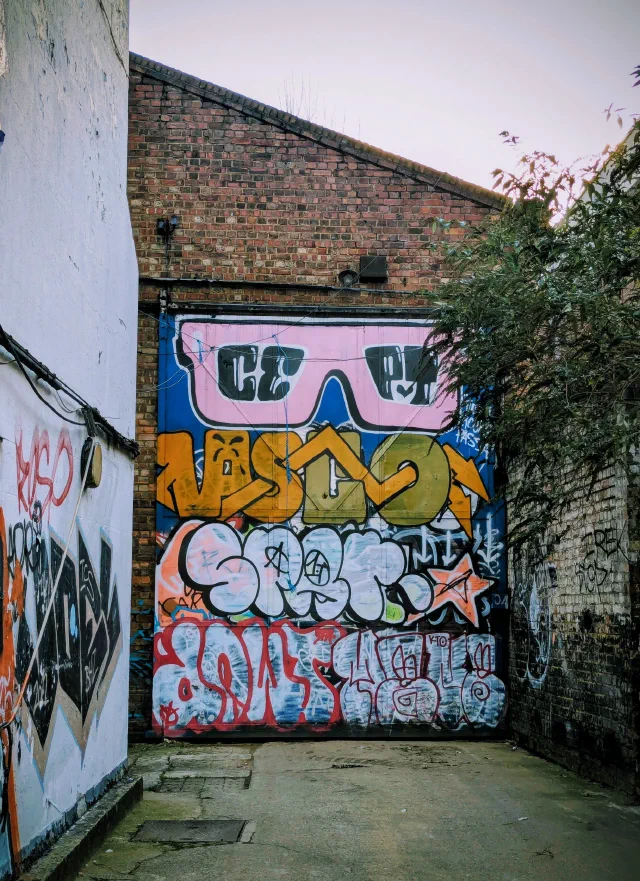 Graffiti lettering stacked up a roller door at the end of an alley, under a giant pair of pink sunglasses with CE PT in the lenses.