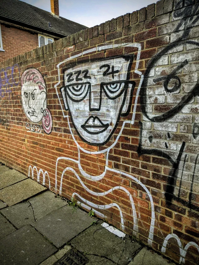 Line-drawn faces in black and white on a red brick wall, one with zzz above its eyes and wavy lines below, another with pink hair and a swirled earring.