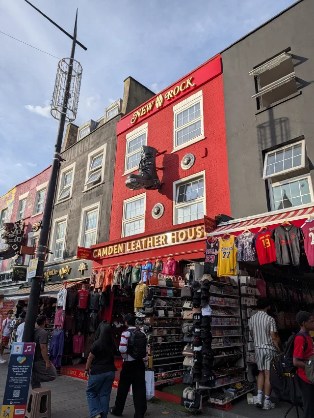 A giant black boot hanging from the red front of Camden Leather House, with football shirts on display below.
