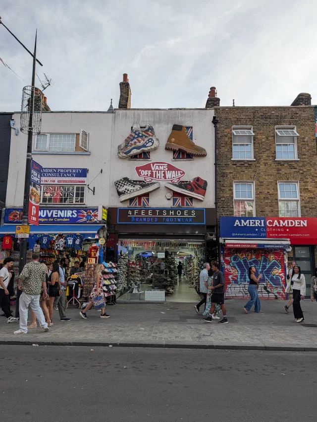 Giant Vans trainers and a work boot on the front of a shoe shop, around a Vans Off the Wall sign, with a graffiti shutter next door.