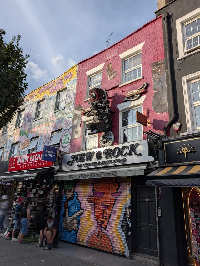 A giant chained boot on the pink front of the New Rock store, next to a building painted with graffiti, and a shutter painted with faces.