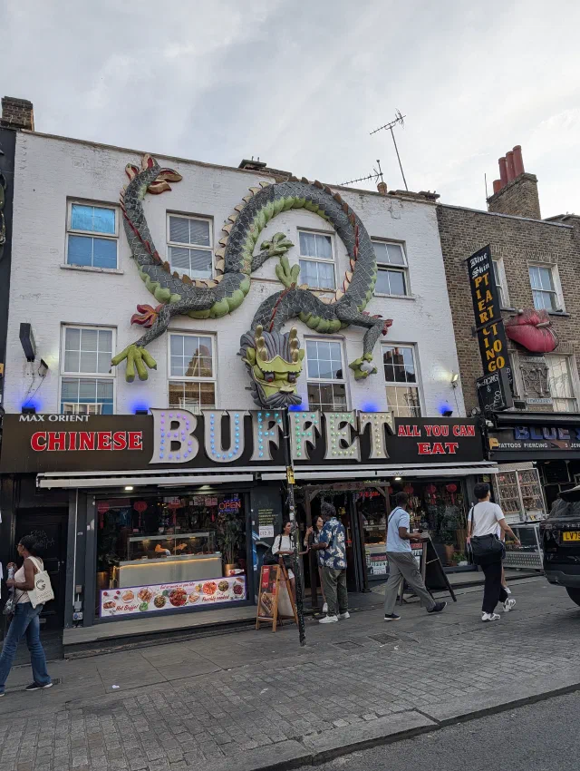 A huge green dragon sculpture coiled across the white front of a Chinese buffet, above a sign in coloured lights.