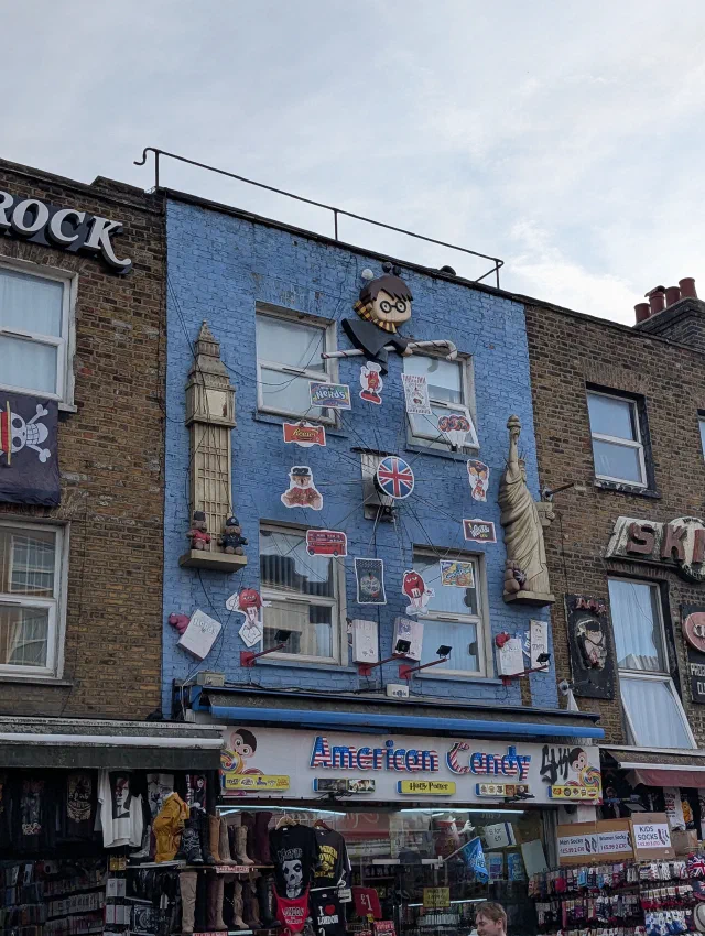 A blue shopfront decorated with sweet wrappers, a Big Ben and Statue of Liberty, and a giant cartoon boy wizard on top.