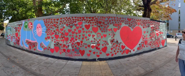 Panorama of a long curved hoarding covered in hundreds of red hearts, with a blue lion, a large heart and the words Grá Gaza.