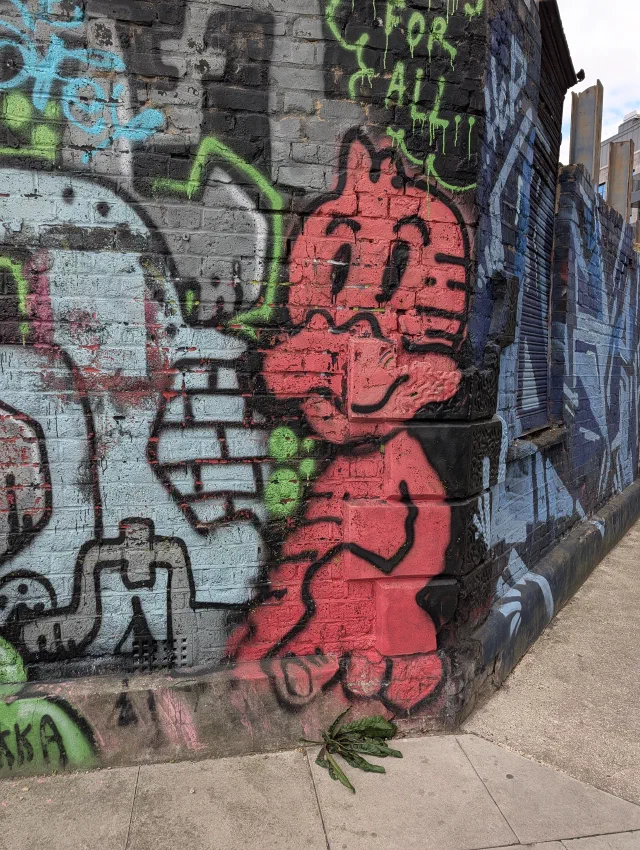 A red cartoon kid with a cheeky grin painted around a corner of a wall, next to a grey toothy character.