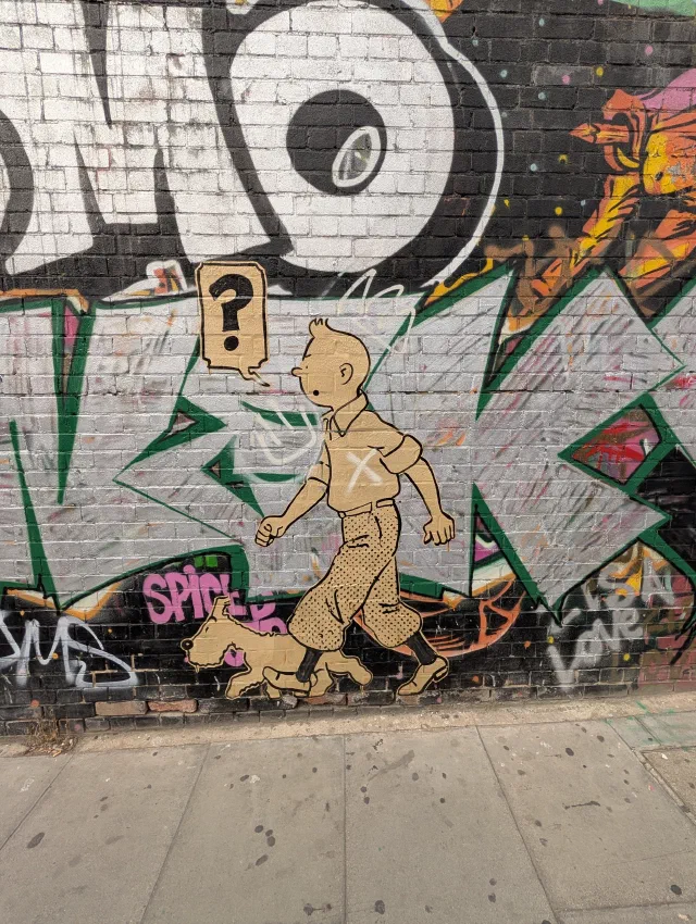 A paste-up of Tintin and Snowy walking along a graffiti wall, with a question mark in a speech bubble.