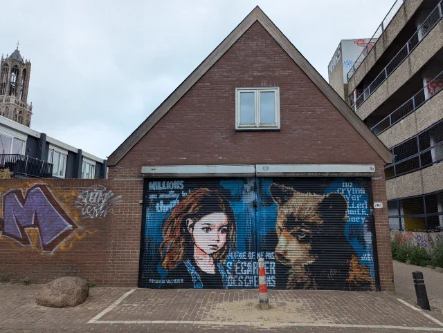A girl with long brown hair painted beside a bear across a garage door with French text, under a brick gable.