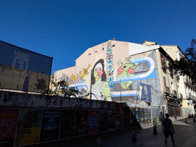 Colourful mural of a woman among swirling shapes, filling the side of a building under a deep blue sky.