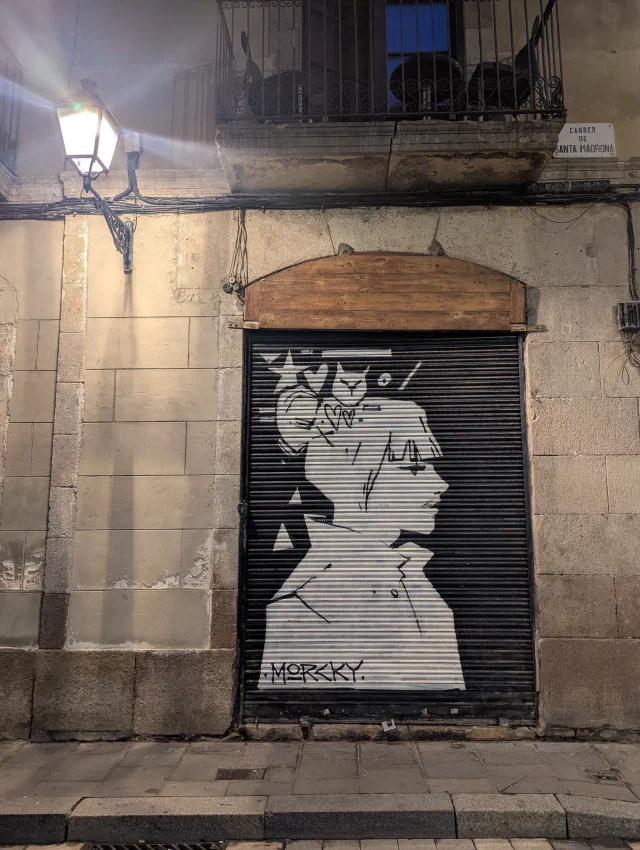 Black and white profile of a woman painted on a metal shutter in an old stone wall, signed Morcky.