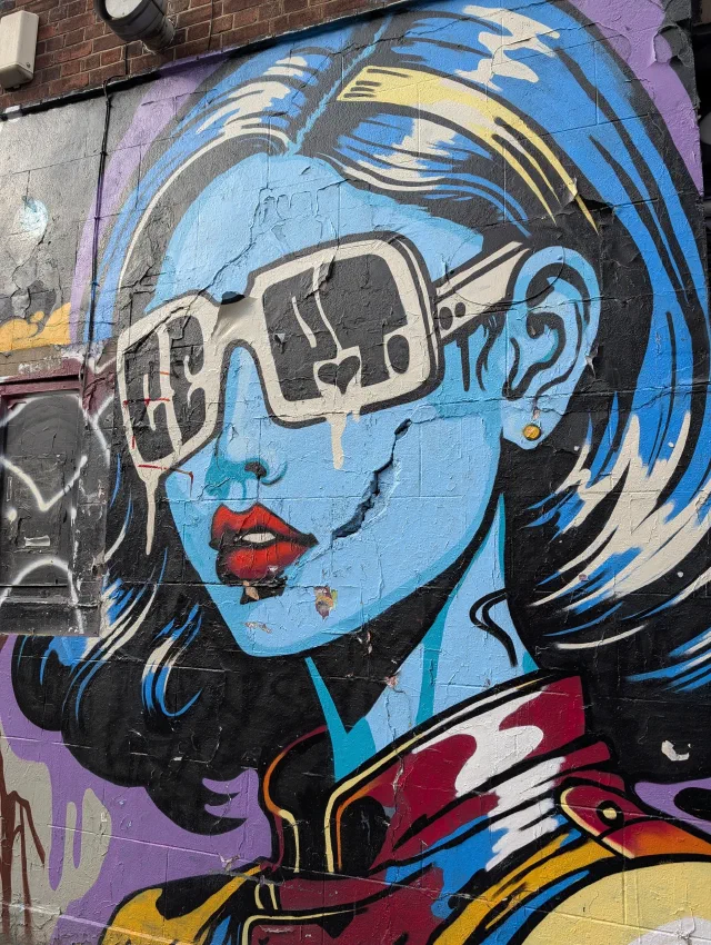 A blue-skinned woman with red lips and oversized white sunglasses, the paint cracked and peeling.