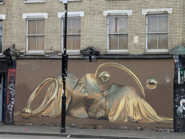 Golden faces with rings and spheres, painted along a shopfront below a row of sash windows.