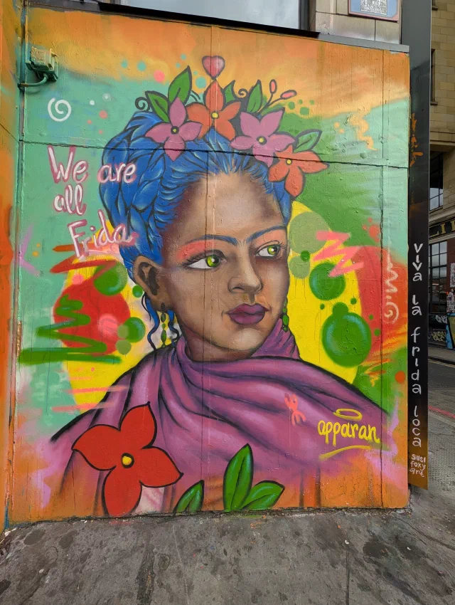 A woman with blue hair, flowers and a purple shawl, with the words We are all Frida, on a panel by a doorway.