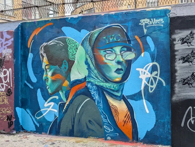 Two women in headscarves and glasses, painted in blues, greens and orange on a wall.