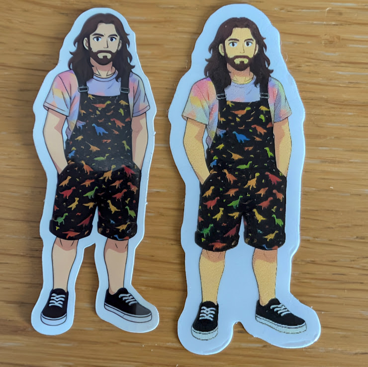Two die-cut stickers on a wooden table showing a bearded person (me) in rainbow T-shirt and black dungarees with colourful dinosaur prints; left from StickerApp and right from StickerShop.