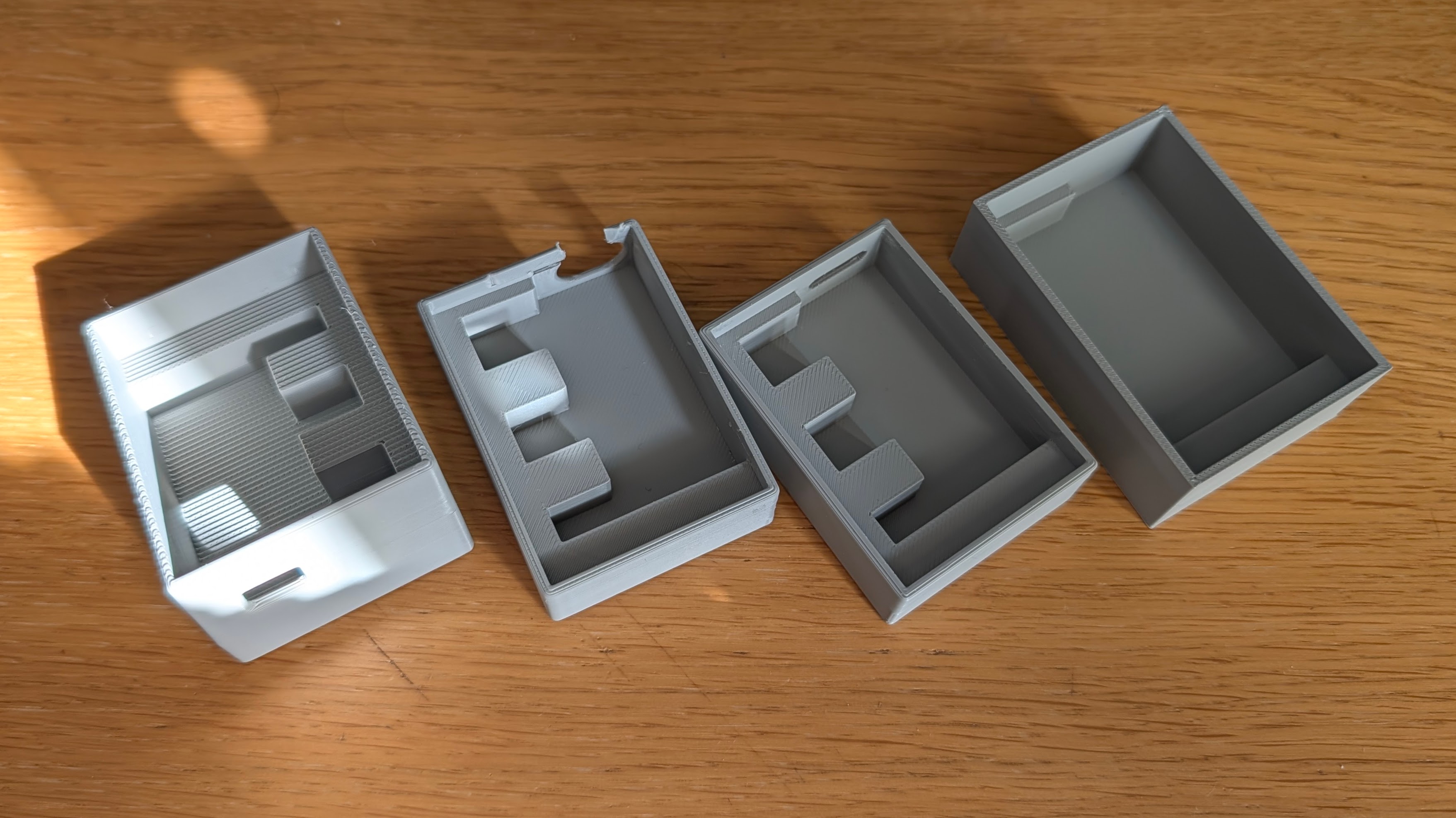 Four grey 3D-printed emailkb stands lined up on a wooden surface, showing the evolution of design.