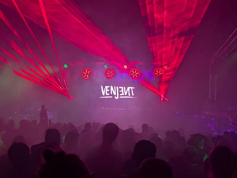 Red laser beams over a crowd in silhouette, with VENJENT on the screen at the back of the stage.
