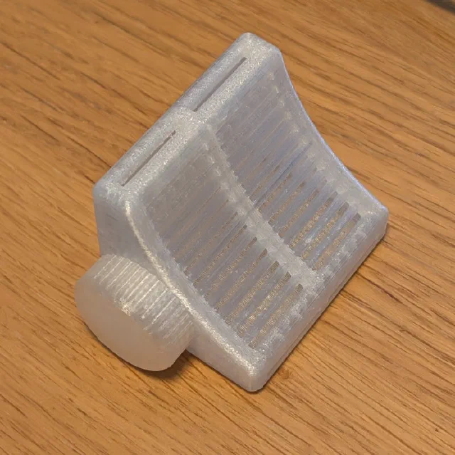 An empty 3D printed desiccant holder in frosted translucent filament on a wooden table. Its curved front is a grid of slots, with a ridged screw-on cap at one end.