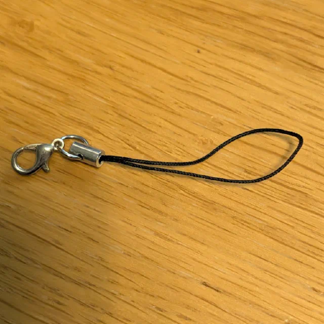 A thin black cord loop on a wooden table, crimped into a small silver metal tube joined by a jump ring to a silver lobster clasp.