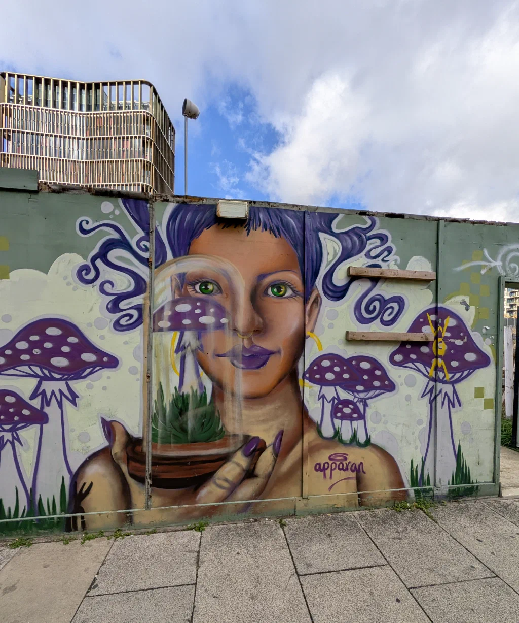 A woman with purple hair and green eyes holding a glass dome over a pot of grass, among purple spotted mushrooms.