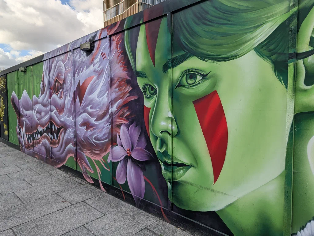 A woman with a green face and a red stripe across her cheek, beside a purple flower and a snarling white dragon.