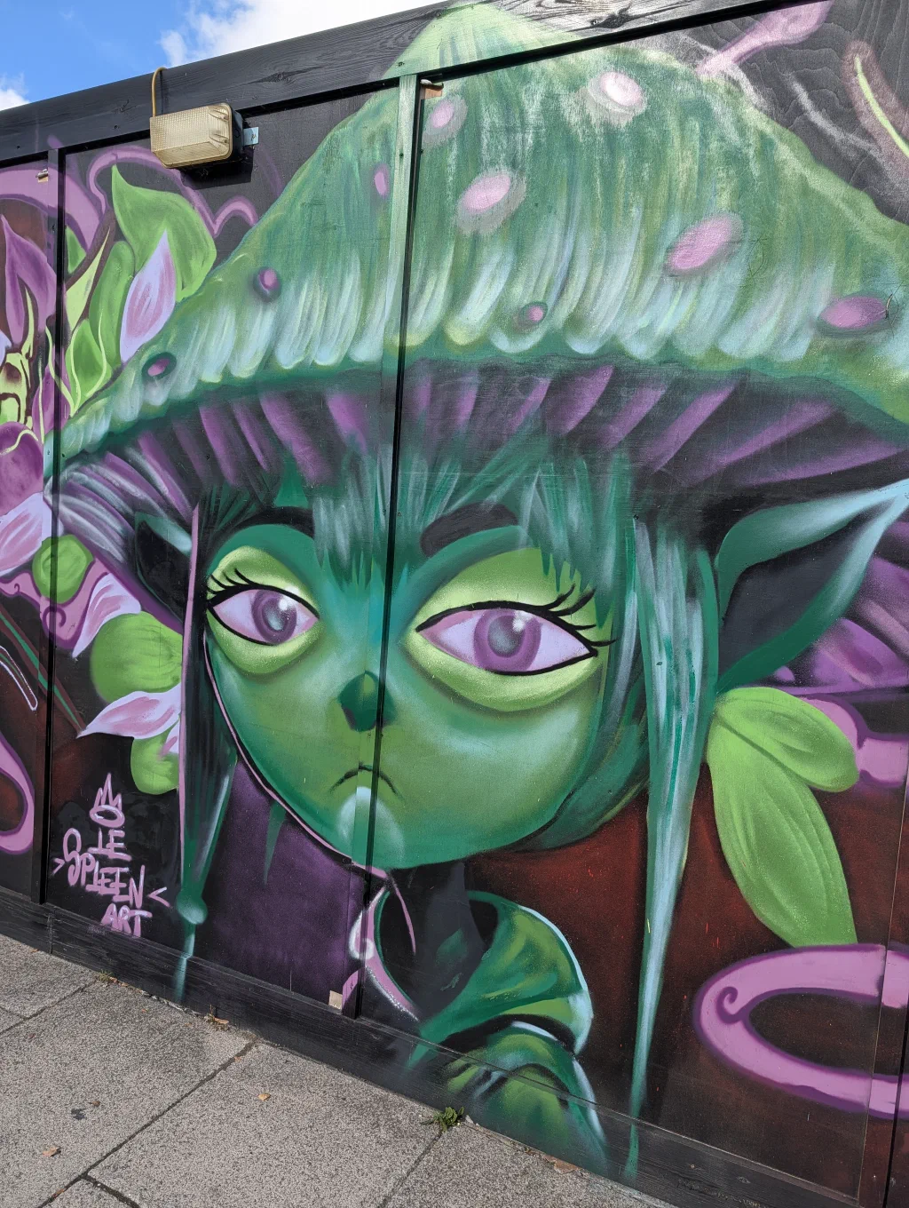 A green-skinned girl with large purple eyes and long green hair under a giant spotted mushroom cap.