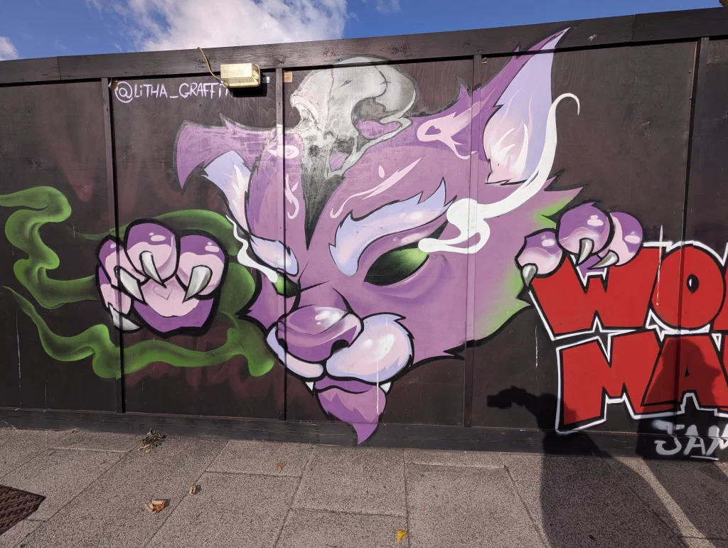 A purple cat with claws out and wisps of white smoke, beside red WOM MAN lettering.