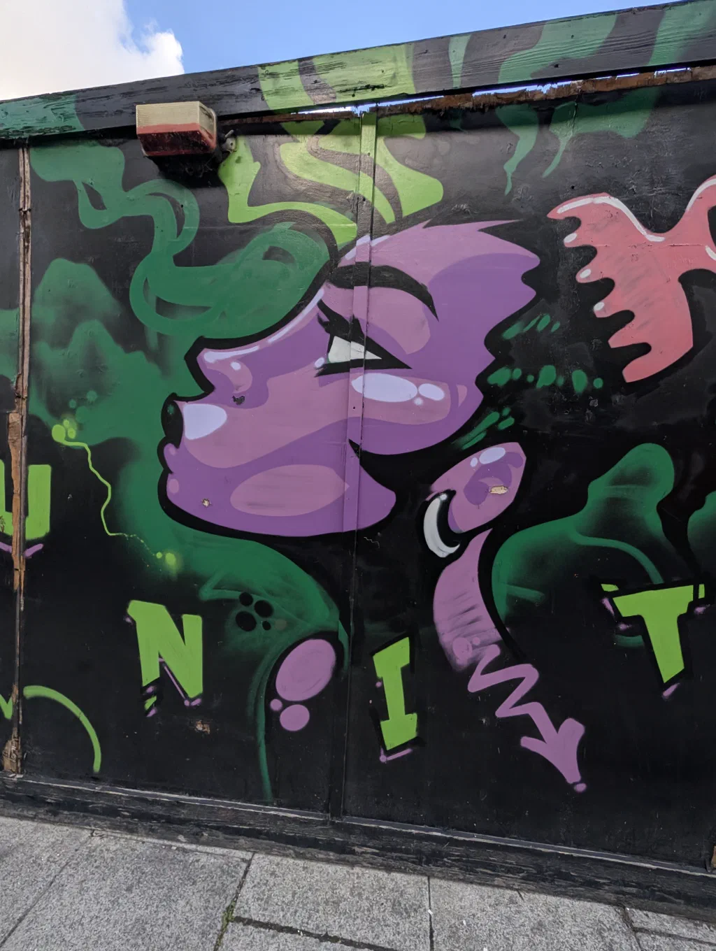 A purple face in profile among green smoke, above green letters spelling UNIT.