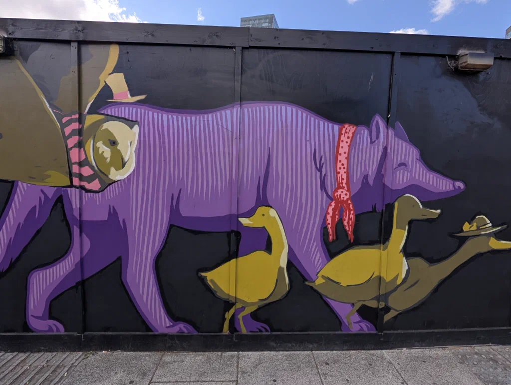 A striped purple wolf with a red spotted scarf walking alongside three yellow geese, one wearing a hat.