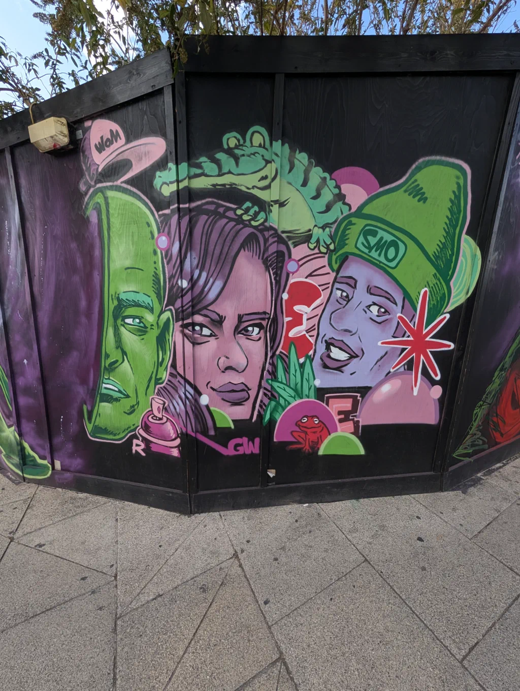 Three cartoon faces, one green, one pink and one in a green beanie, with a crocodile lying across the top.