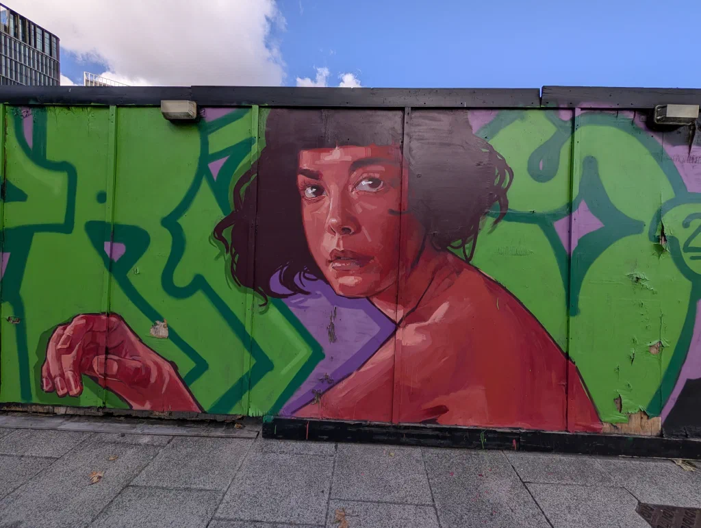A woman with short dark hair in a red top, painted in shades of red over green graffiti letters.