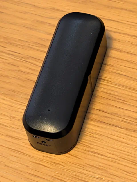 The ZG-IR01 IR blaster on a wooden table: a small black pill-shaped box with a glossy top, two small windows on the end and a reset pinhole labelled RESET.